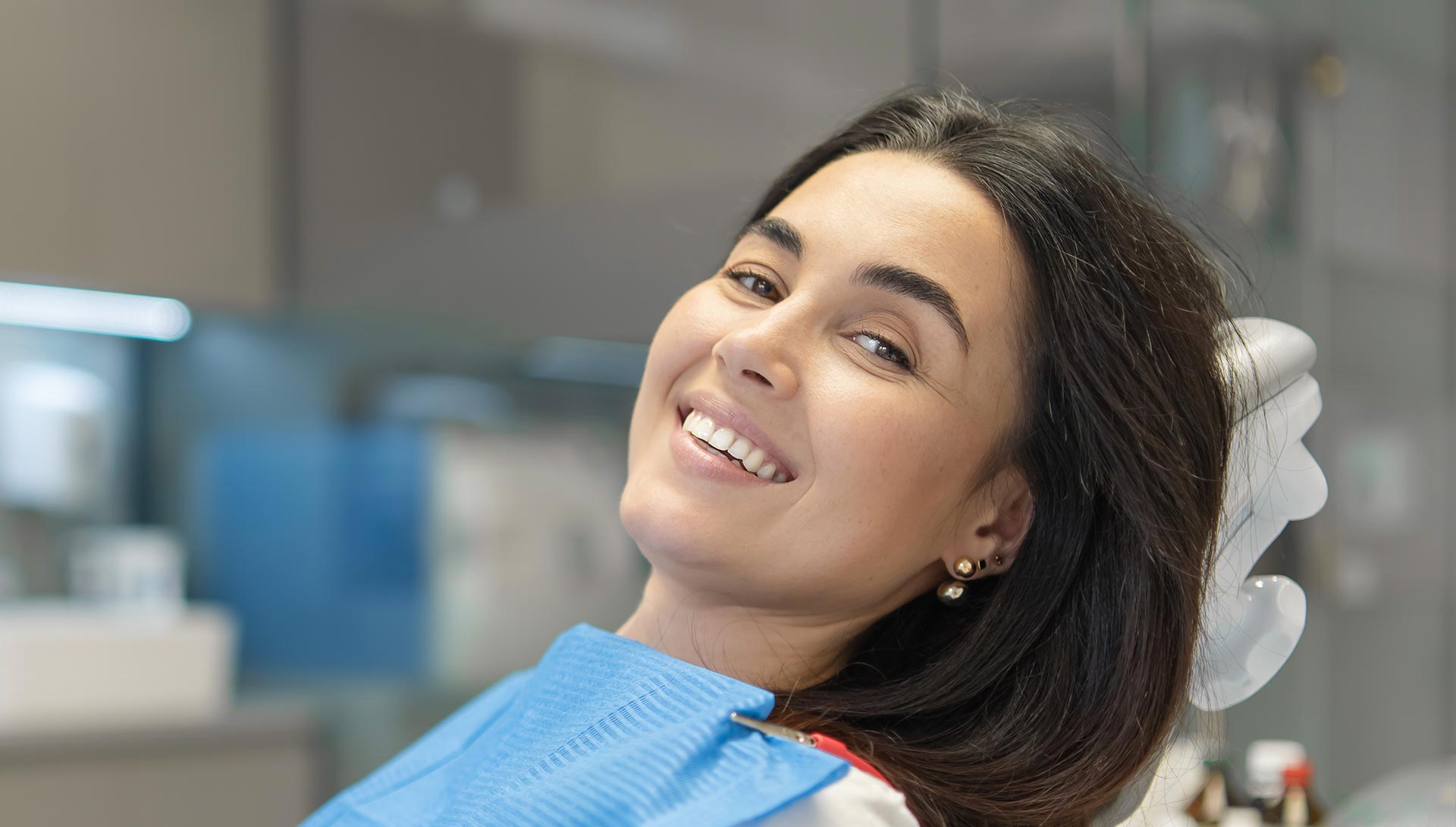 A woman with dark hair smiling at the camera while sitting in a dental chair.